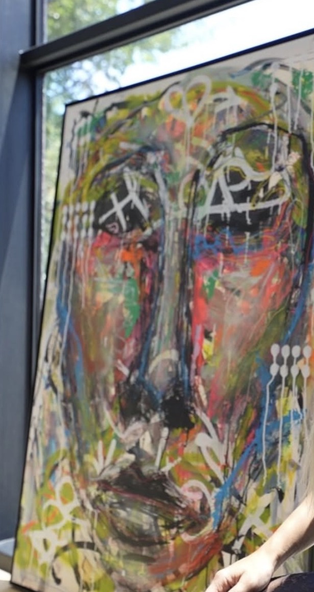 Large face painting in graffiti marks, drips and raw colour, leaning against a window.