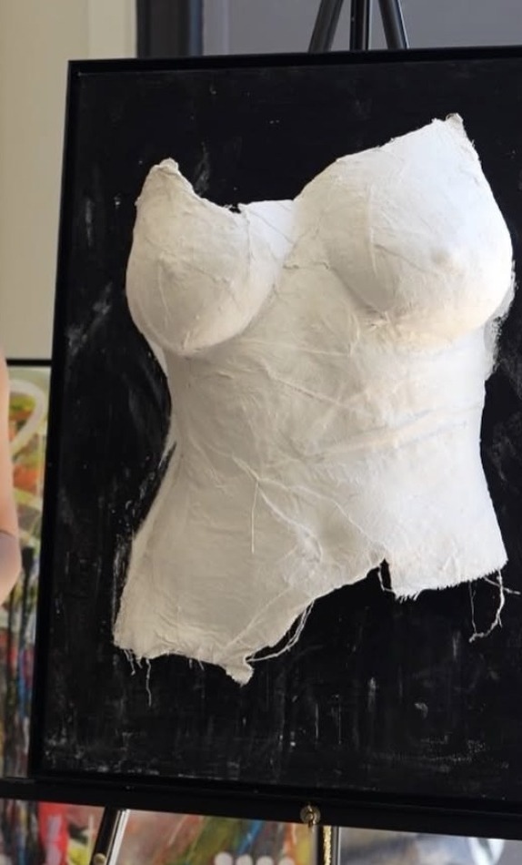 White plaster torso cast on a black ground, standing on a studio easel.